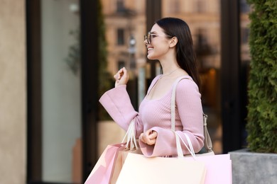 Happy woman with colorful shopping bags outdoors, space for text