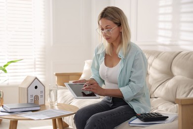 Photo of Budget planning. Woman using tablet on sofa indoors