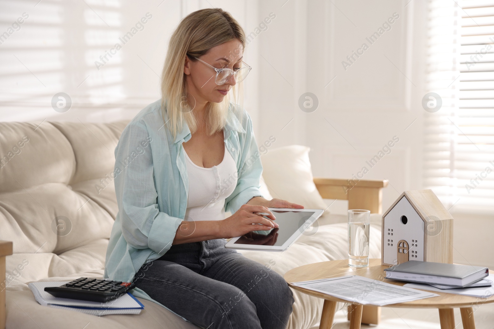 Photo of Budget planning. Woman using tablet on sofa indoors