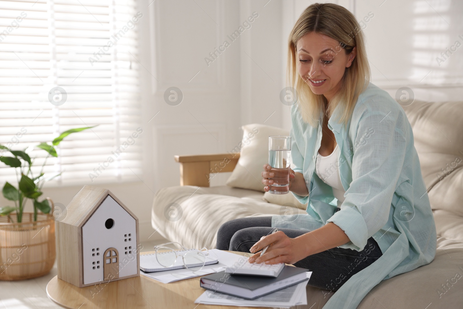 Photo of Budget planning. Woman with glass of water using calculator at table indoors