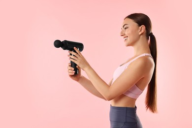 Young woman with percussive massager on pink background