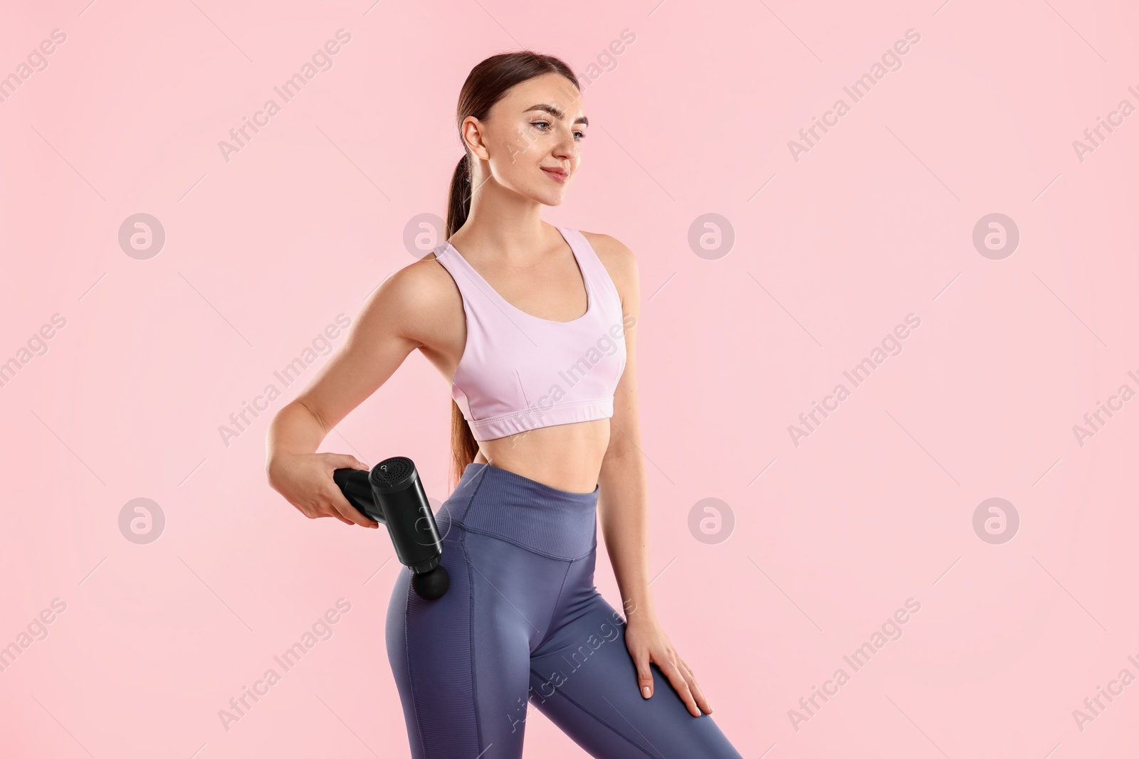 Photo of Woman using percussive massager to relax hip muscles on pink background