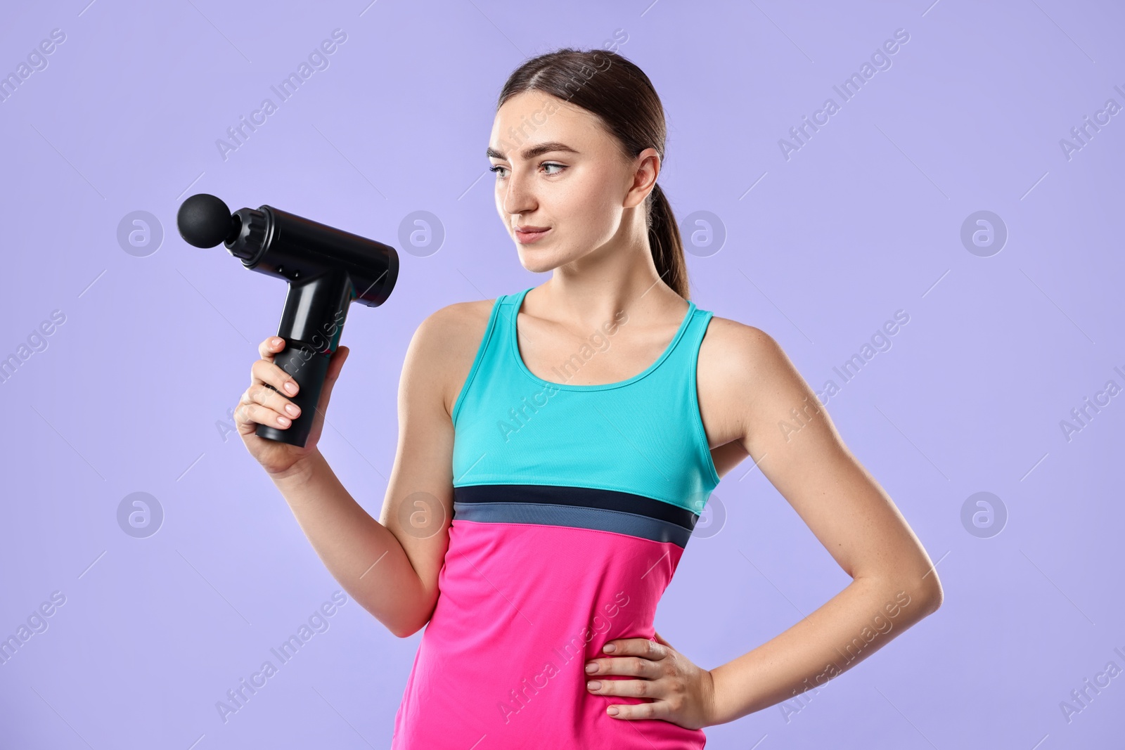 Photo of Young woman with percussive massager on light purple background