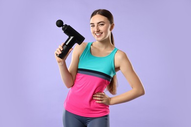 Young woman with percussive massager on light purple background