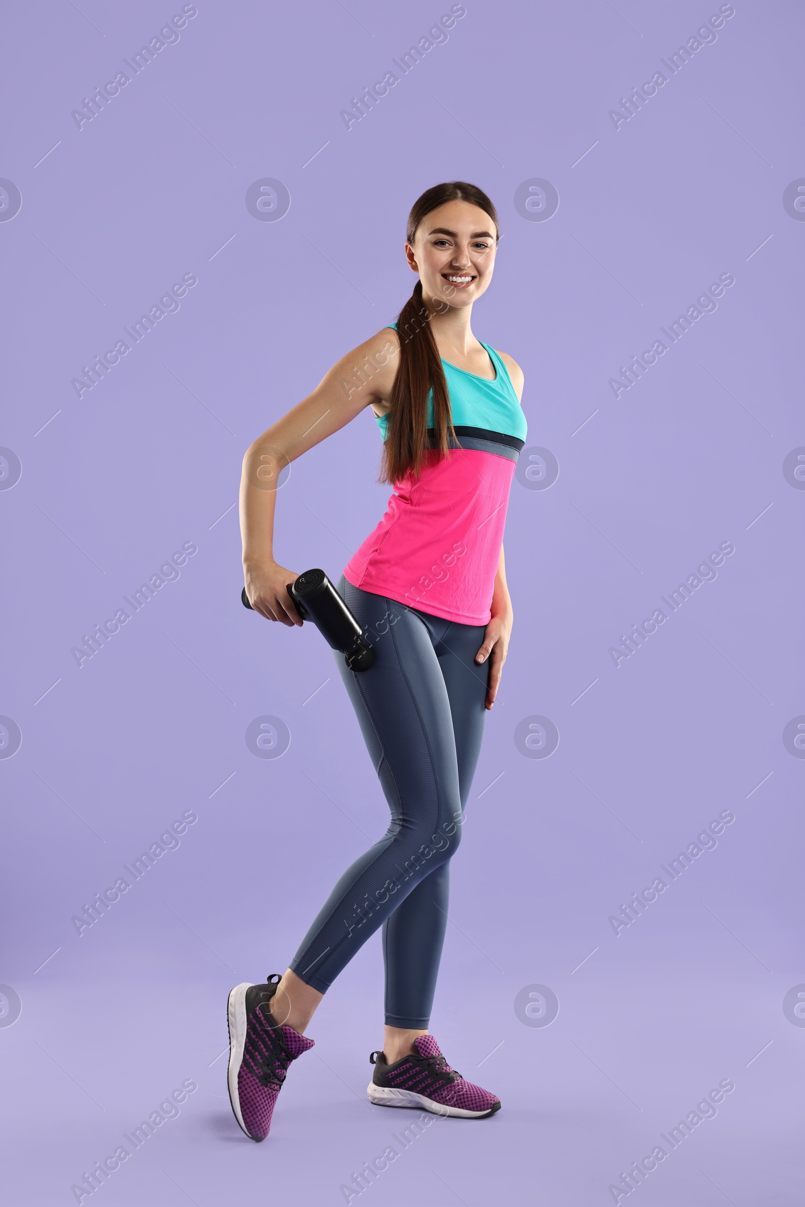 Photo of Woman using percussive massager to relax hip muscles on light purple background