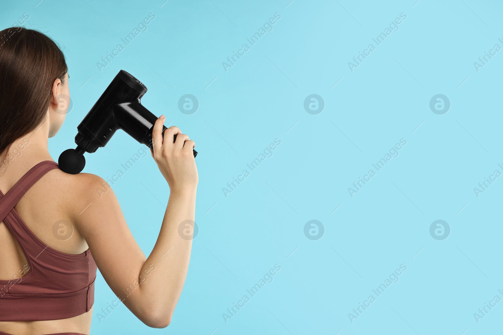 Photo of Woman using percussive massager to relieve trapezius muscle on light blue background, back view. Space for text