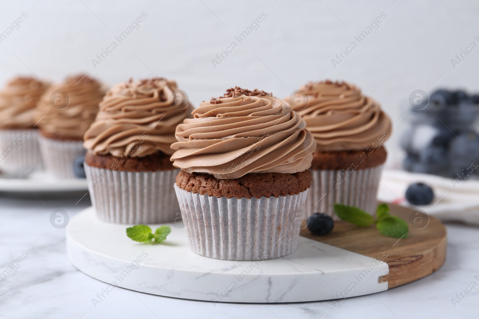 Photo of Tasty cupcakes with chocolate cream and blueberries on white marble table, closeup