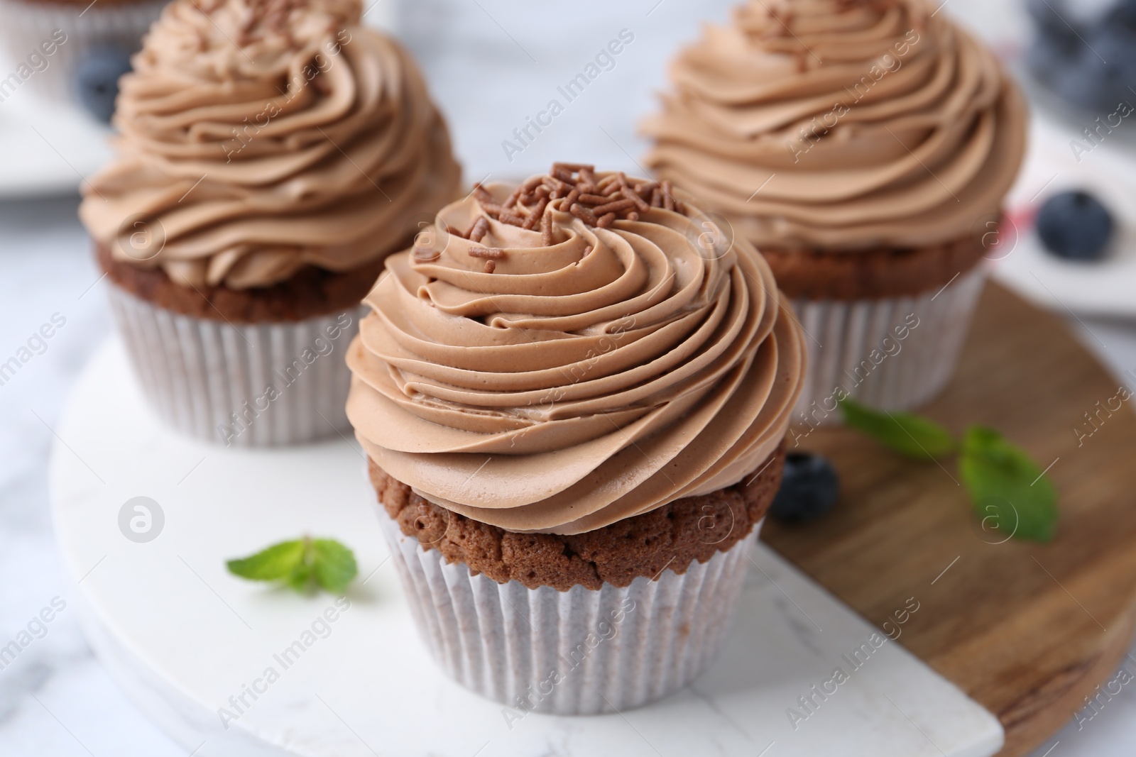 Photo of Tasty cupcakes with chocolate cream and blueberries on white marble table, closeup