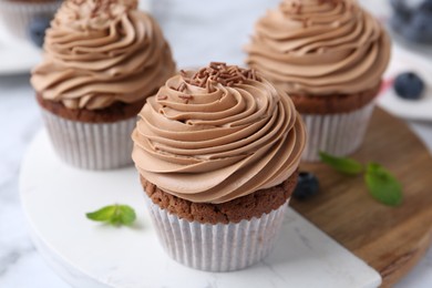 Photo of Tasty cupcakes with chocolate cream and blueberries on white marble table, closeup