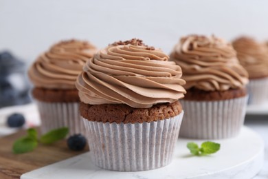 Photo of Tasty cupcakes with chocolate cream and blueberries on table, closeup