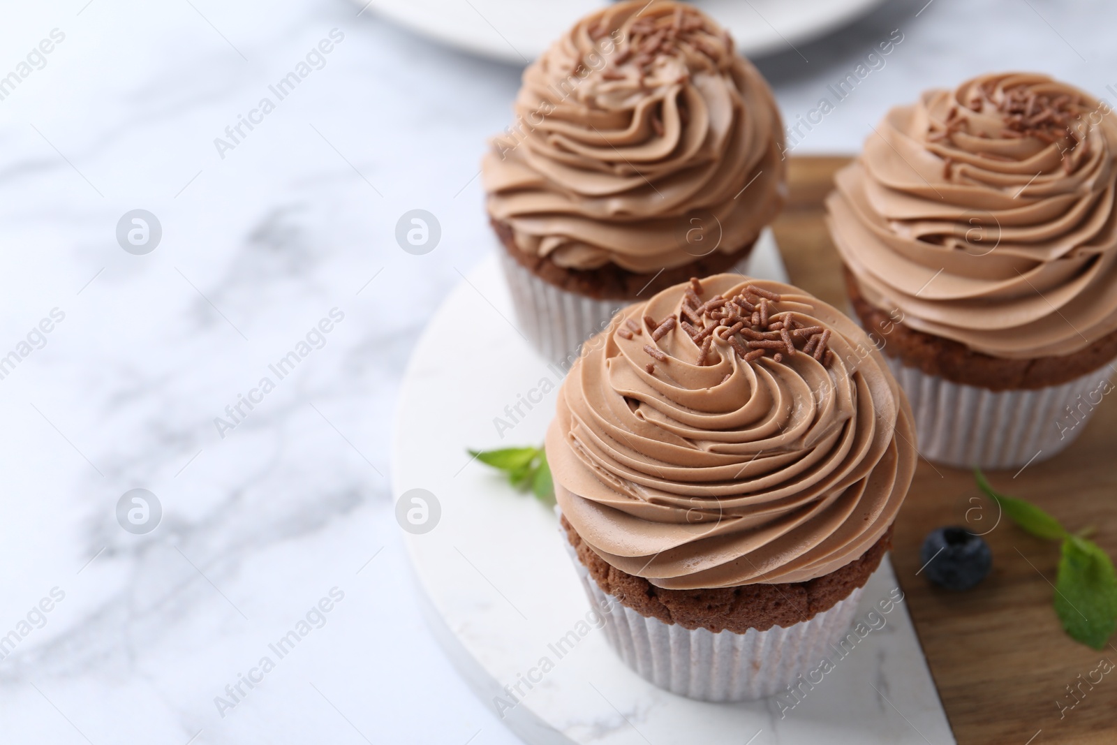 Photo of Tasty cupcakes with chocolate cream on white marble table, closeup. Space for text