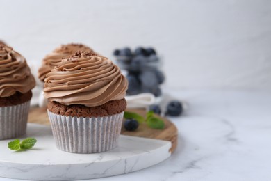 Photo of Tasty cupcakes with chocolate cream and blueberries on white marble table, closeup. Space for text