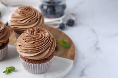 Photo of Tasty cupcakes with chocolate cream and blueberries on white marble table, closeup. Space for text