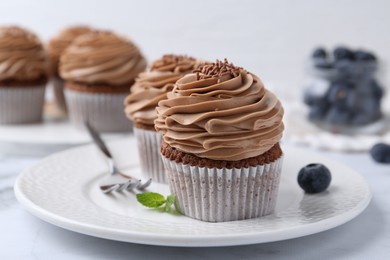 Photo of Tasty cupcakes with chocolate cream and blueberries on white marble table, closeup