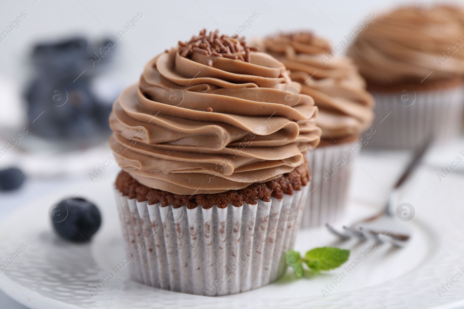 Photo of Tasty cupcakes with chocolate cream and blueberries on table, closeup