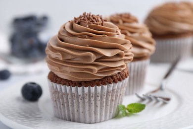 Photo of Tasty cupcakes with chocolate cream and blueberries on table, closeup