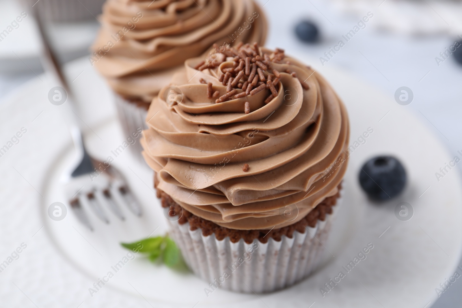 Photo of Tasty cupcakes with chocolate cream and blueberries on table, closeup