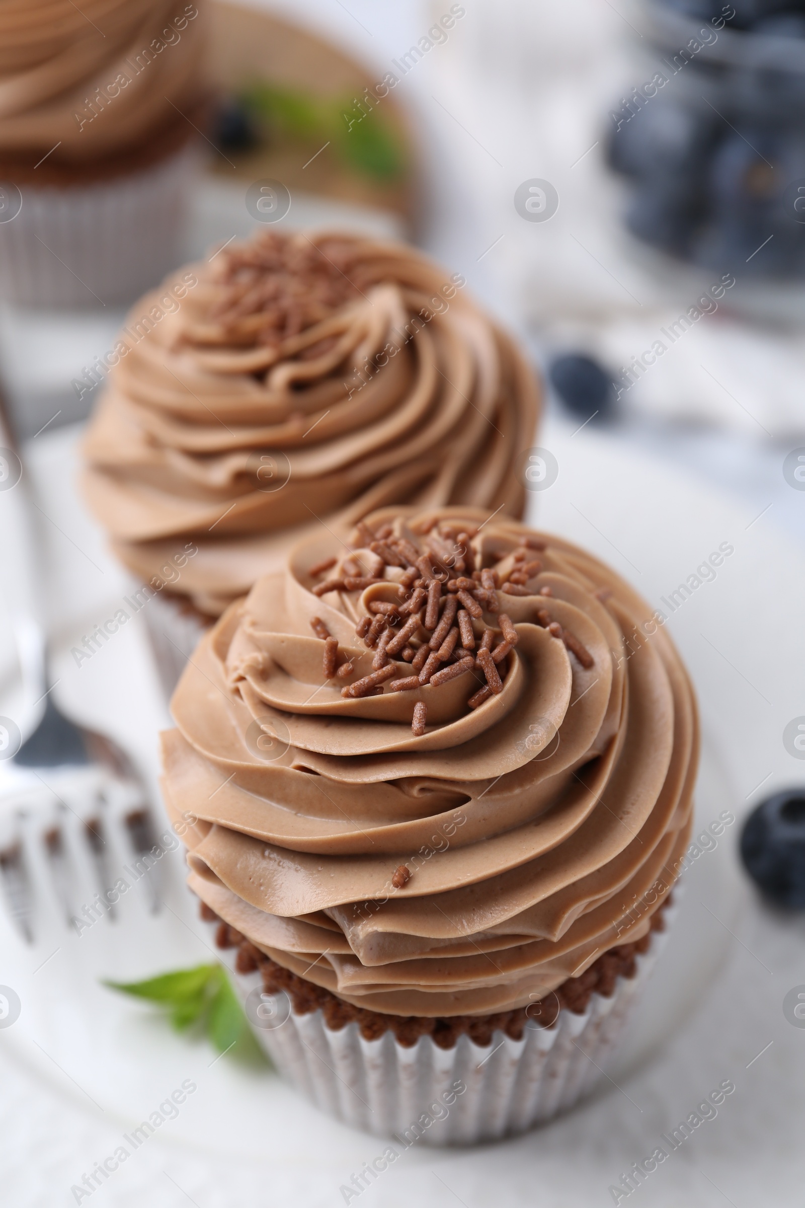 Photo of Tasty cupcakes with chocolate cream and blueberries on table, closeup