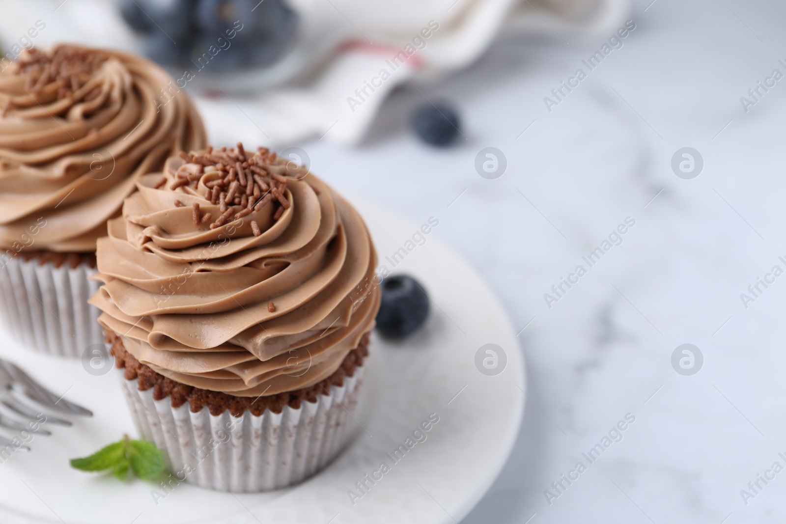 Photo of Tasty cupcakes with chocolate cream and blueberries on white marble table, closeup. Space for text