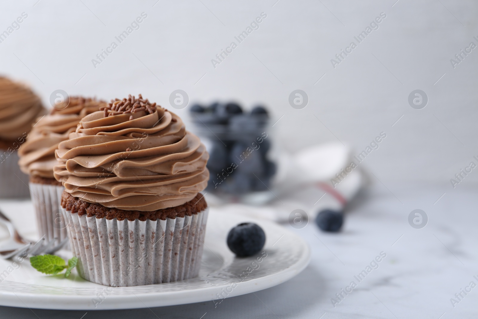 Photo of Tasty cupcakes with chocolate cream and blueberries on white marble table, closeup. Space for text