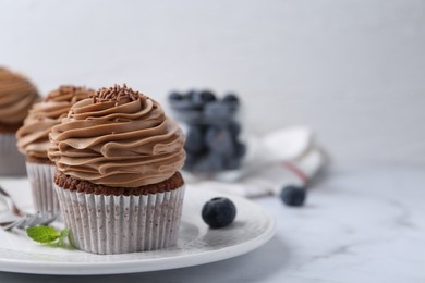 Photo of Tasty cupcakes with chocolate cream and blueberries on white marble table, closeup. Space for text