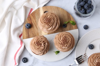 Photo of Tasty cupcakes with chocolate cream and blueberries on white marble table, flat lay