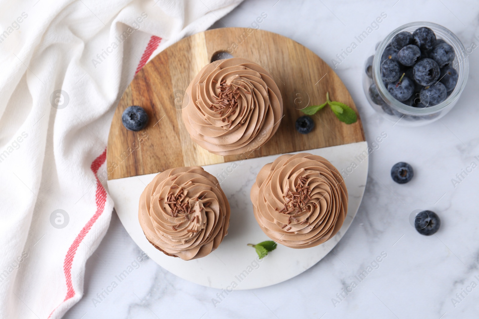 Photo of Tasty cupcakes with chocolate cream and blueberries on white marble table, flat lay