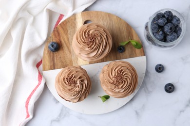 Photo of Tasty cupcakes with chocolate cream and blueberries on white marble table, flat lay