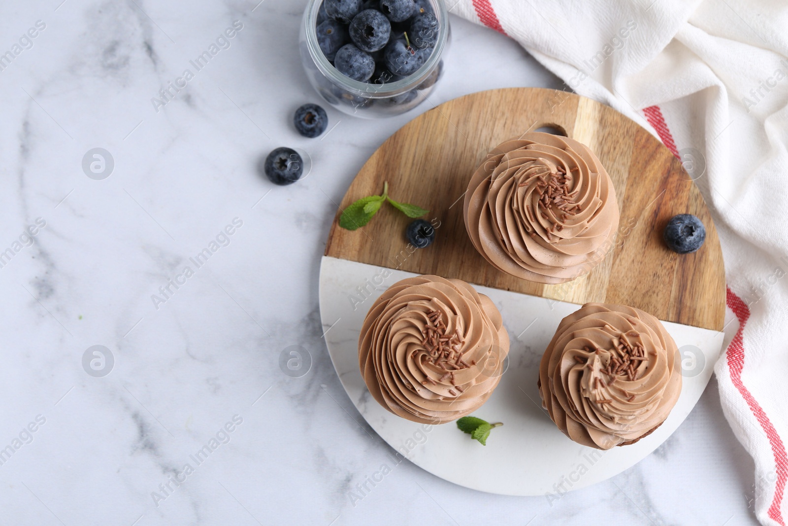 Photo of Tasty cupcakes with chocolate cream and blueberries on white marble table, flat lay. Space for text