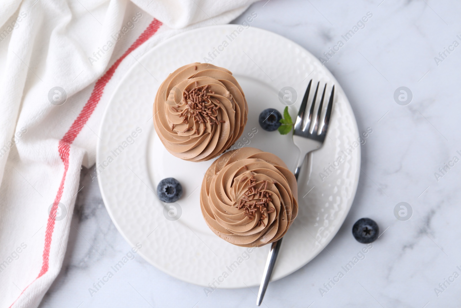 Photo of Tasty cupcakes with chocolate cream and blueberries on white marble table, top view