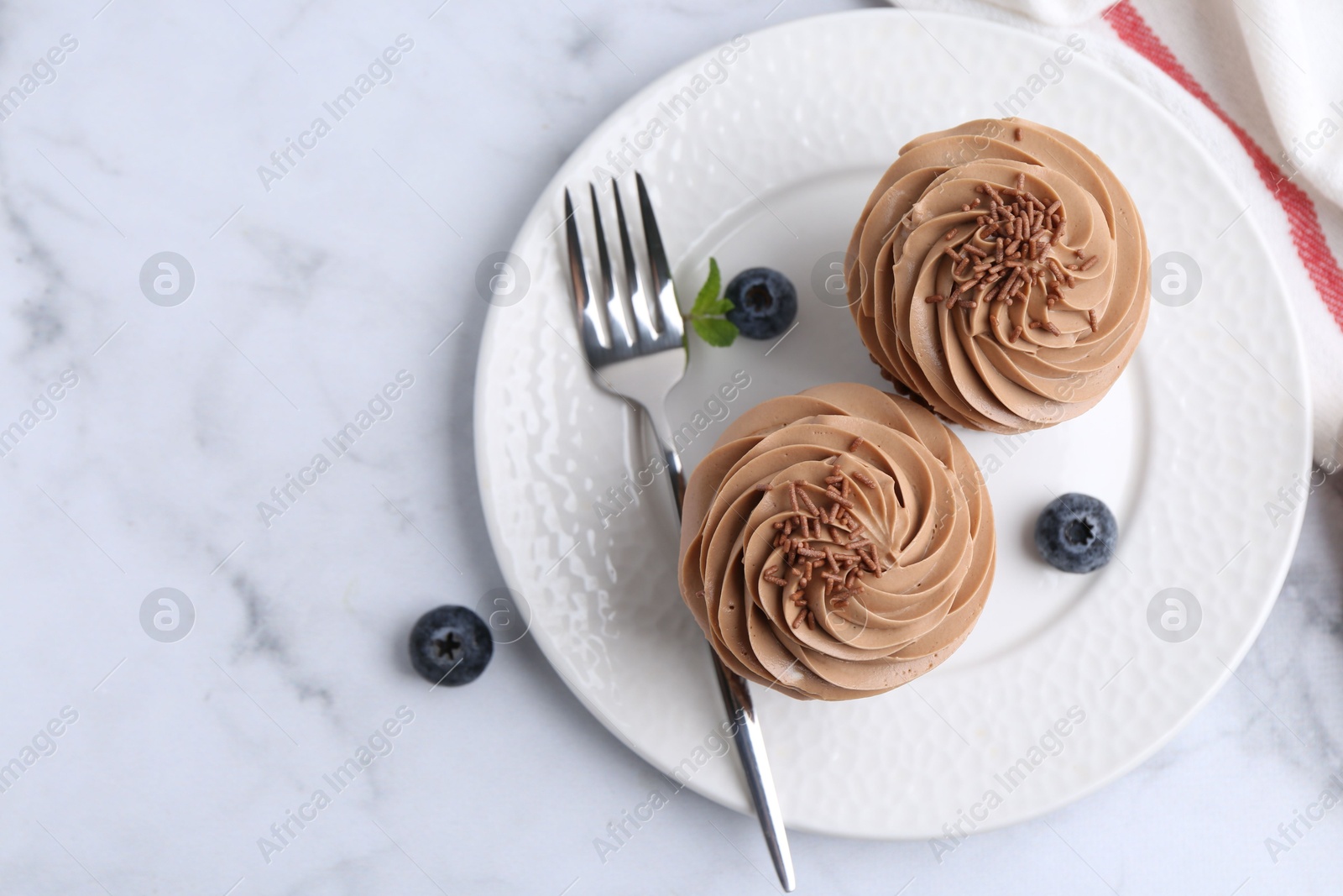 Photo of Tasty cupcakes with chocolate cream and blueberries on white marble table, top view. Space for text