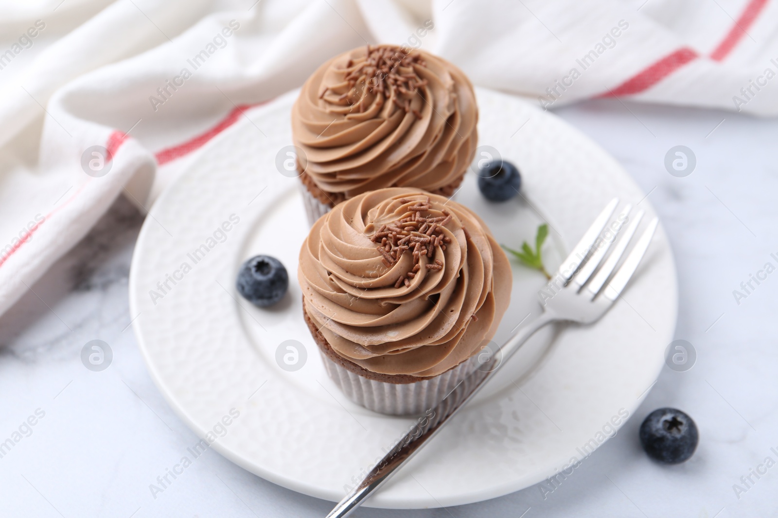 Photo of Tasty cupcakes with chocolate cream and blueberries on white marble table