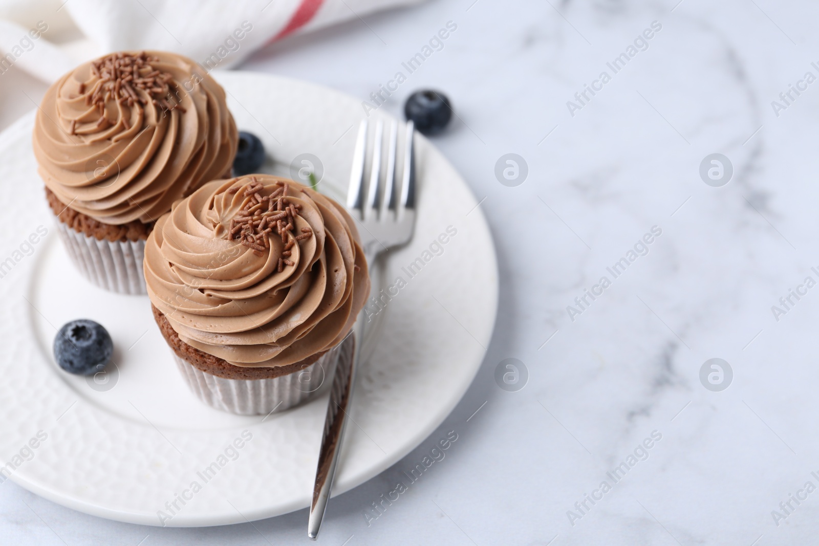 Photo of Tasty cupcakes with chocolate cream and blueberries on white marble table, space for text