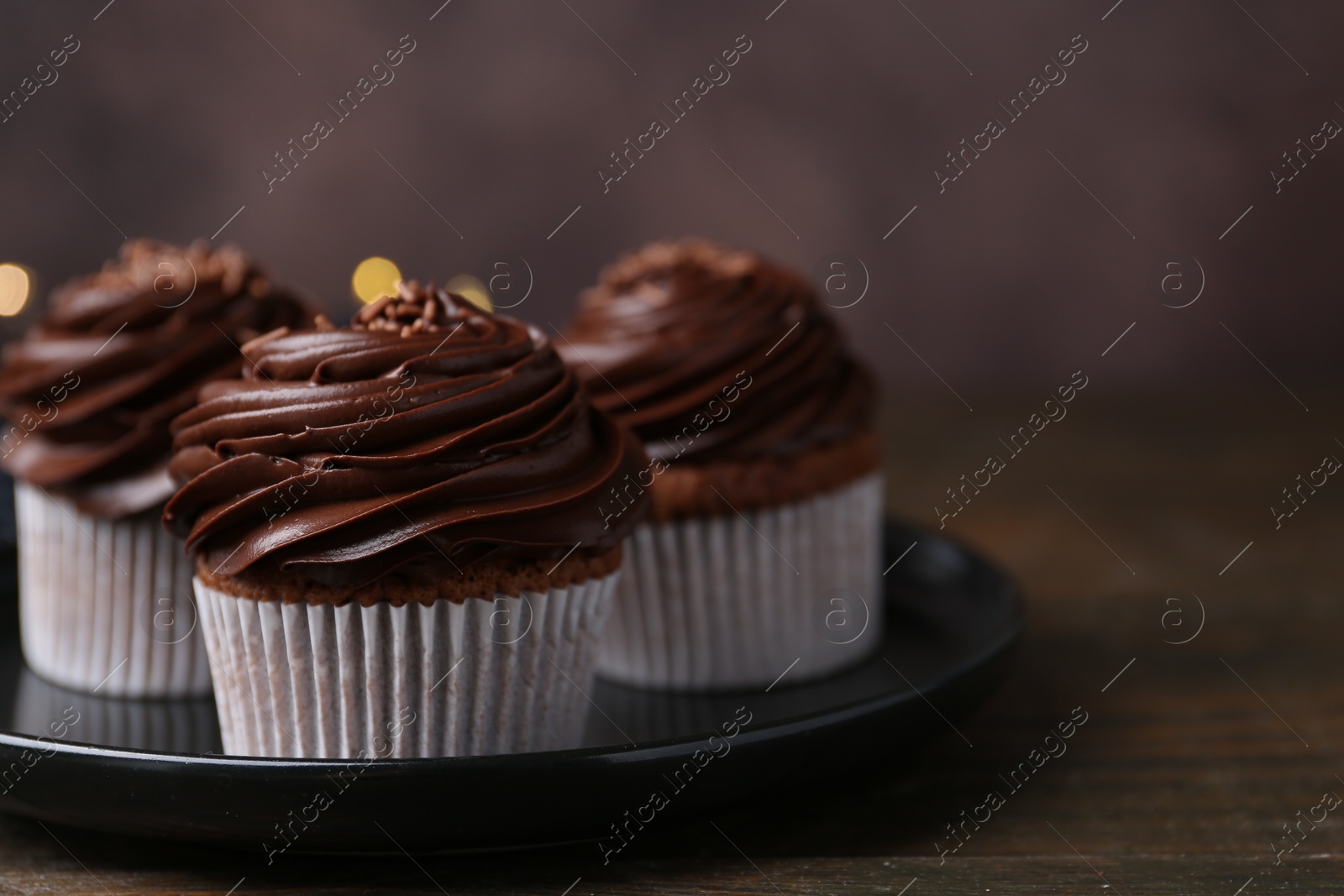 Photo of Tasty cupcakes with chocolate cream on wooden table, closeup. Space for text