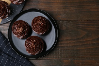 Photo of Tasty cupcakes with chocolate cream on wooden table, top view. Space for text