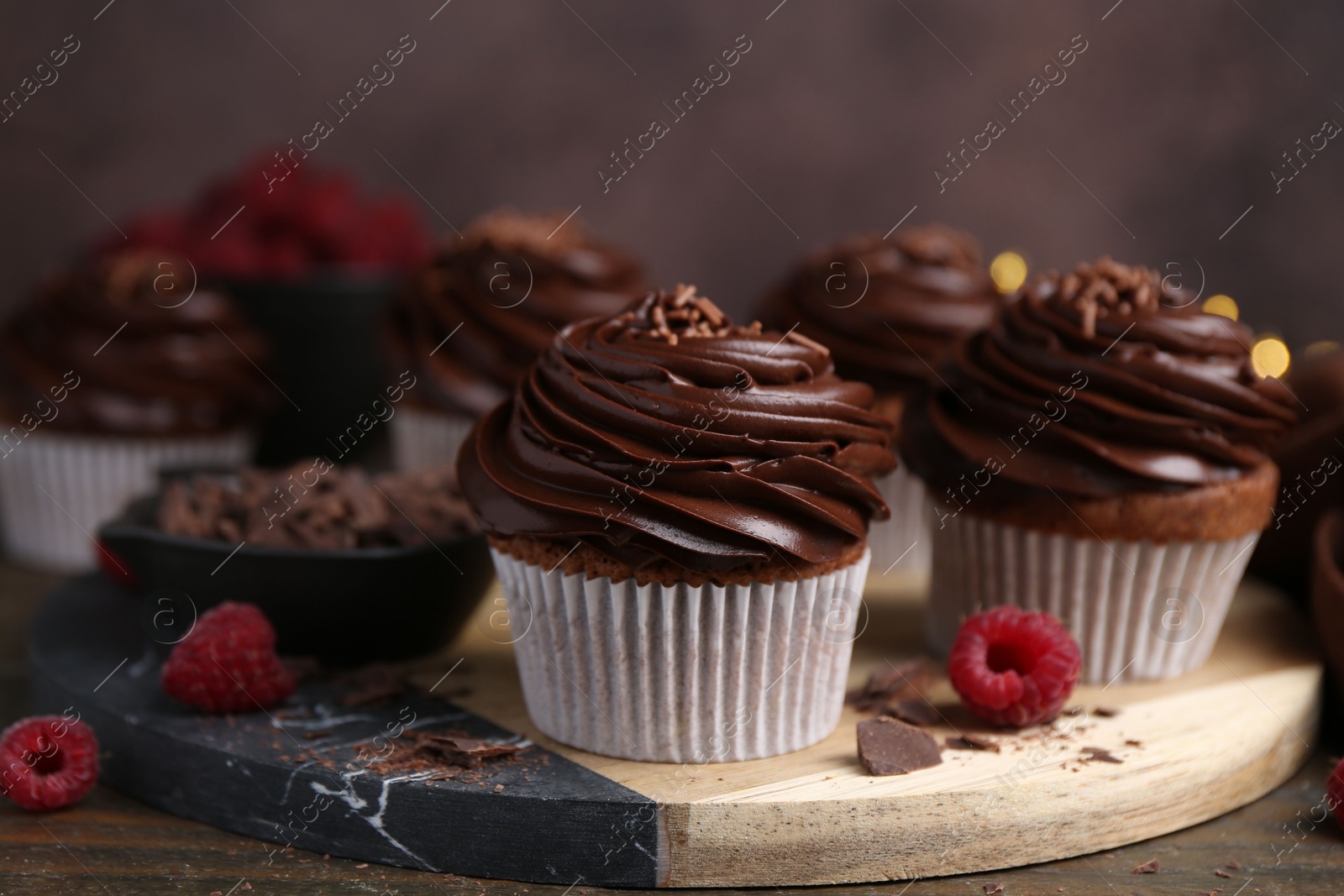 Photo of Tasty cupcakes with chocolate cream and raspberries on wooden table, closeup