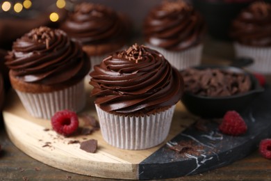 Photo of Tasty cupcakes with chocolate cream and raspberries on wooden table, closeup