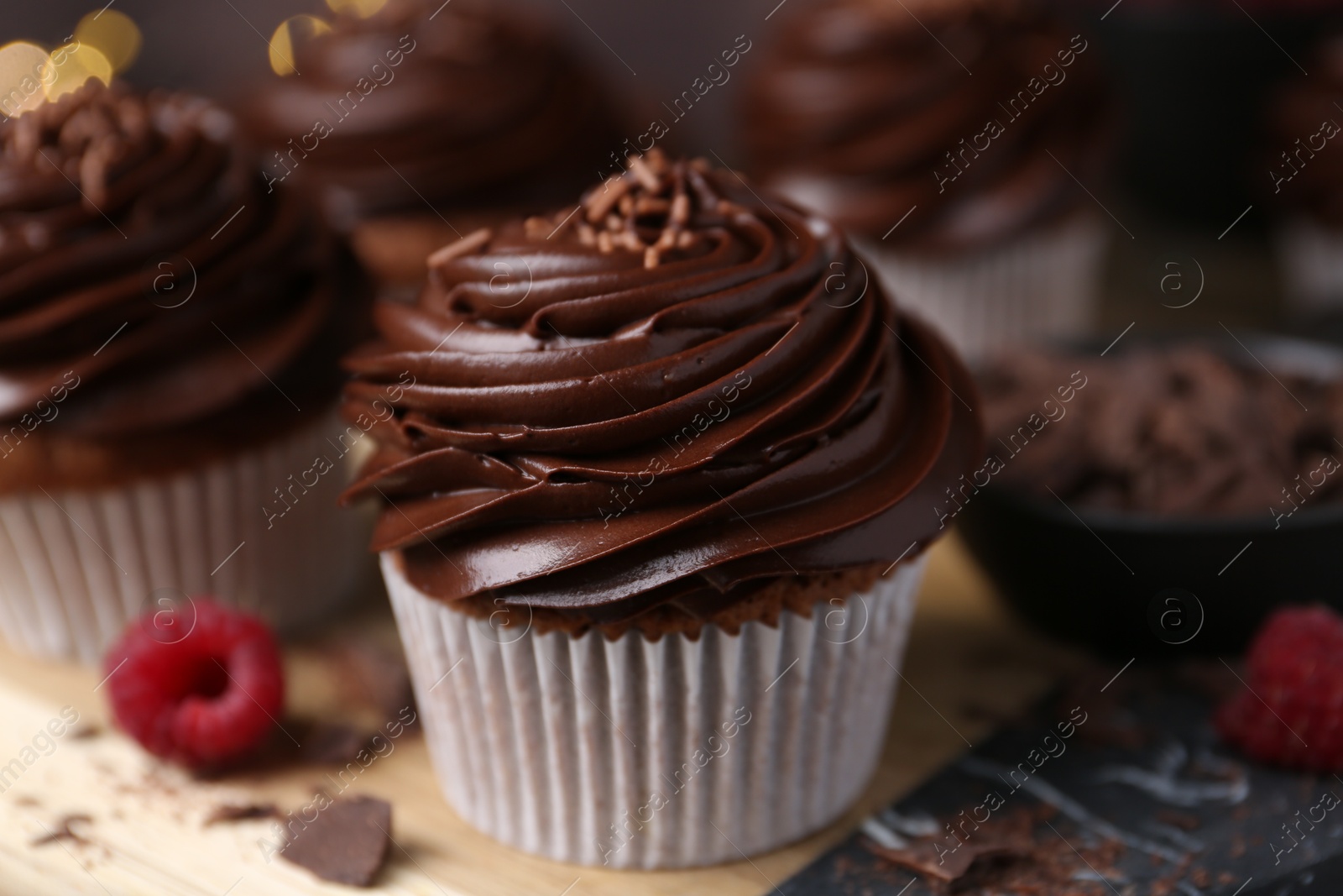 Photo of Tasty cupcakes with chocolate cream and raspberries on wooden table, closeup