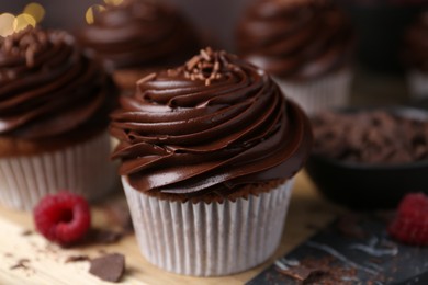 Photo of Tasty cupcakes with chocolate cream and raspberries on wooden table, closeup