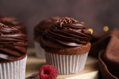 Photo of Tasty cupcakes with chocolate cream and raspberries on wooden table, closeup