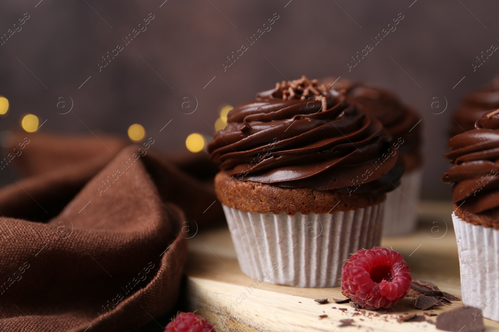 Photo of Tasty cupcakes with chocolate cream and raspberries on wooden table, closeup