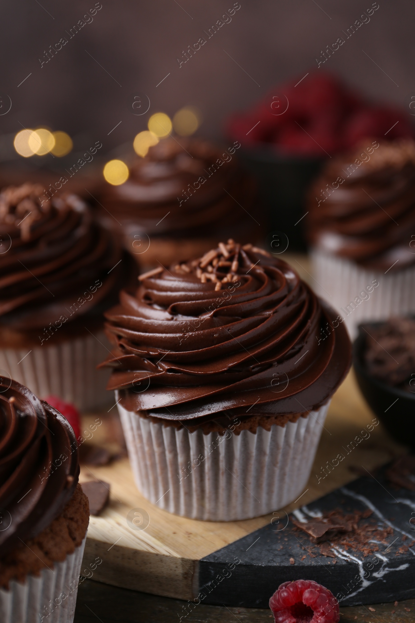 Photo of Tasty cupcakes with chocolate cream and raspberries on wooden table, closeup