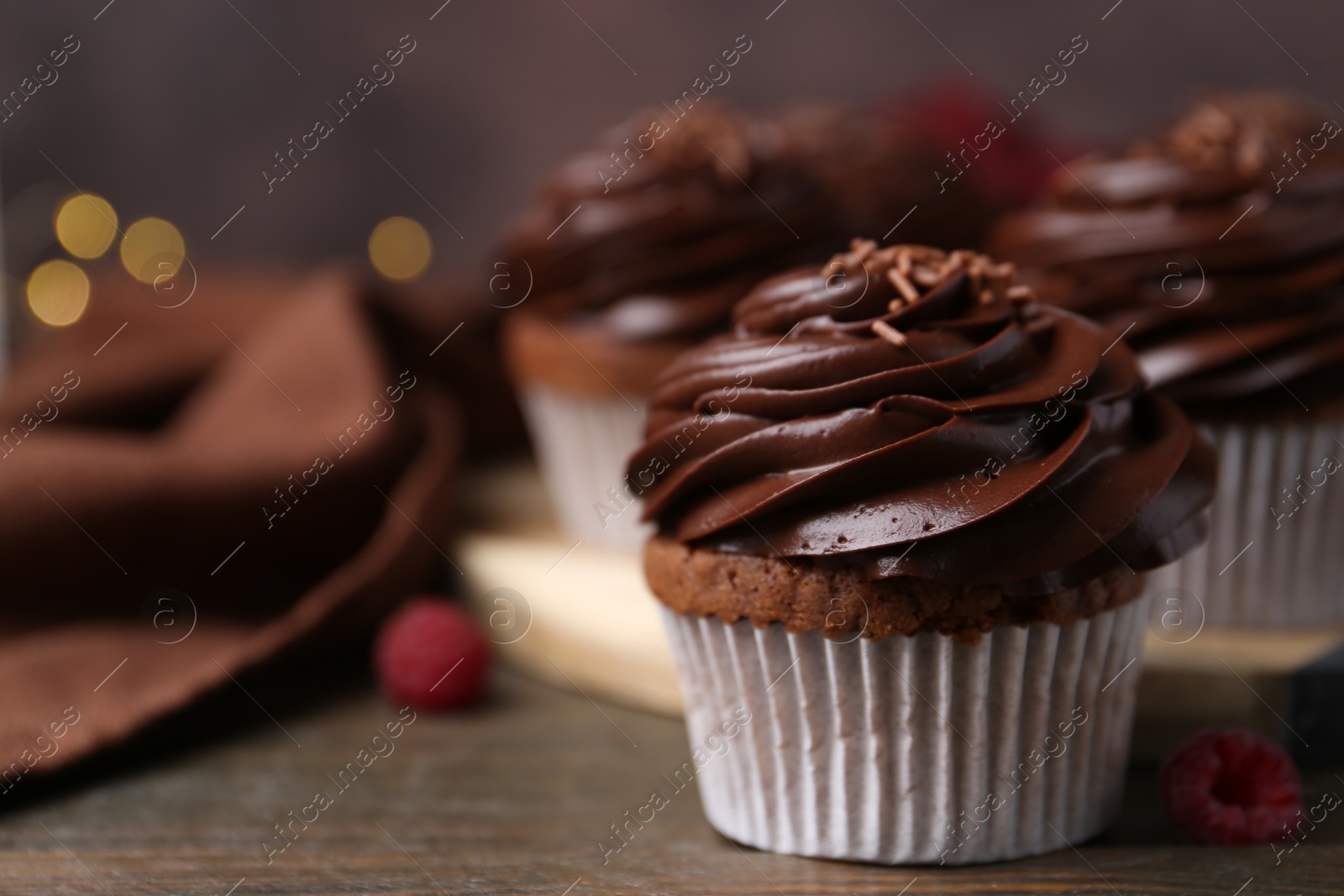 Photo of Tasty cupcakes with chocolate cream and raspberries on wooden table, closeup. Space for text