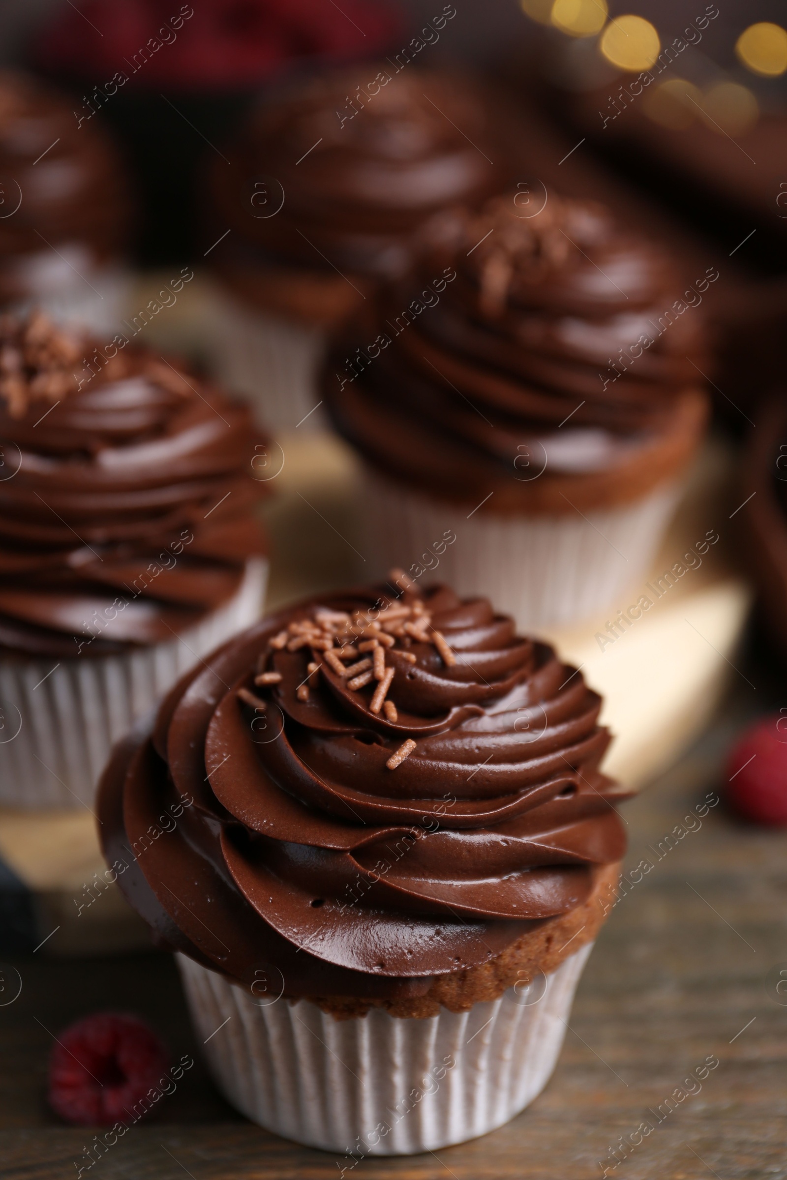 Photo of Tasty cupcakes with chocolate cream and raspberries on wooden table, closeup