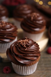 Photo of Tasty cupcakes with chocolate cream and raspberries on wooden table, closeup