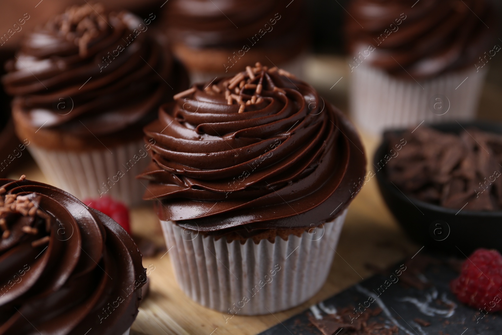 Photo of Tasty cupcakes with chocolate cream and raspberries on wooden table, closeup