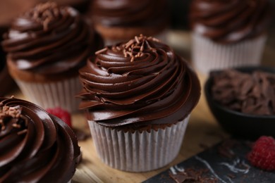 Photo of Tasty cupcakes with chocolate cream and raspberries on wooden table, closeup