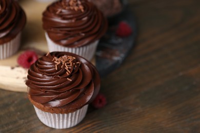 Photo of Tasty cupcakes with chocolate cream and raspberries on wooden table, closeup. Space for text