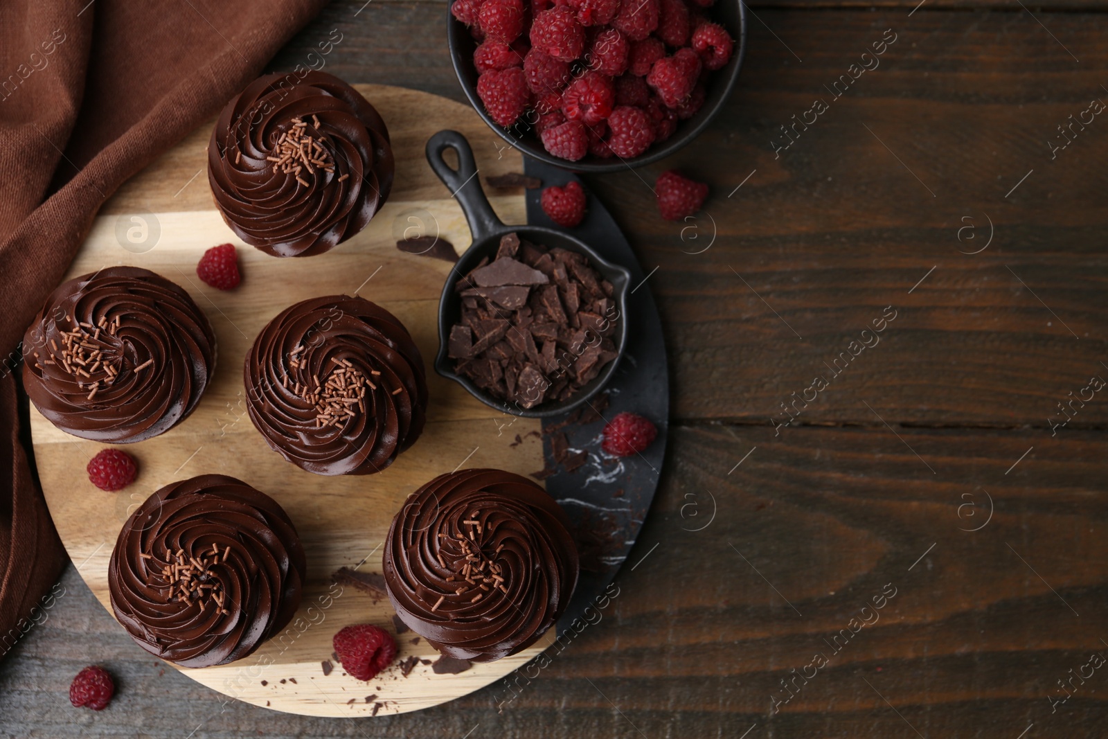 Photo of Tasty cupcakes with chocolate cream and raspberries on wooden table, flat lay. Space for text