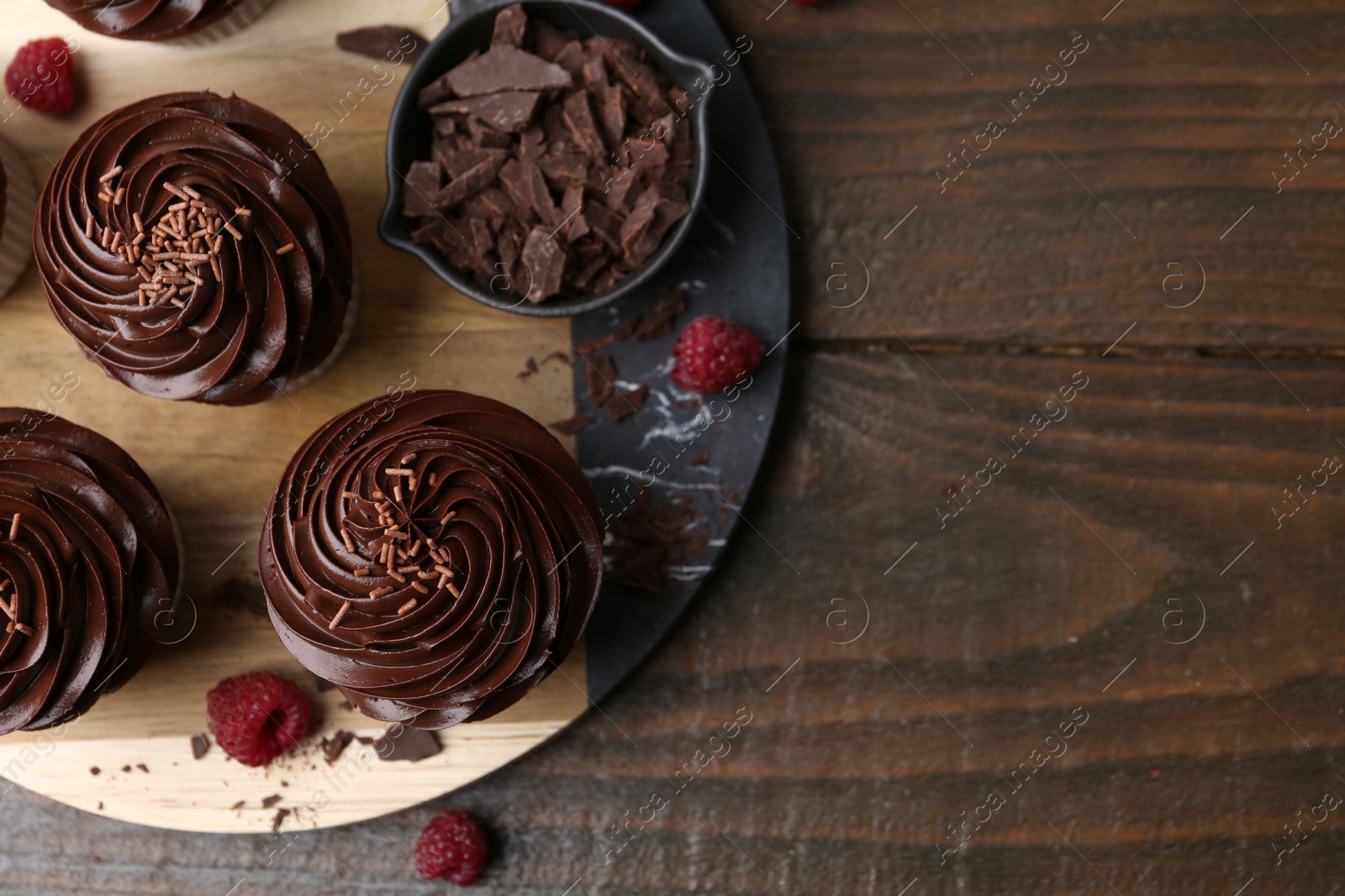 Photo of Tasty cupcakes with chocolate cream and raspberries on wooden table, flat lay. Space for text